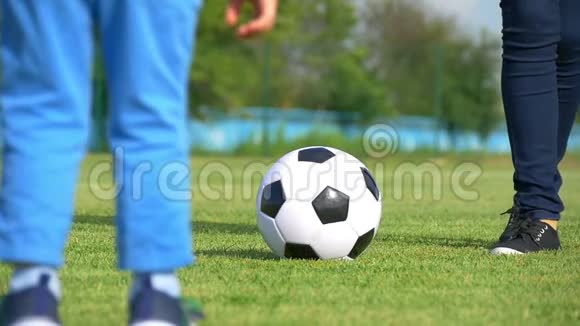 一个年轻的女人和孩子的腿在体育场的绿色草坪上缓慢的特写镜头中玩足球这就是视频的预览图