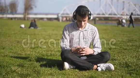 一个人坐在草地上的公园里在蓝牙上听科学家的音乐学生微笑唱歌跳舞视频的预览图