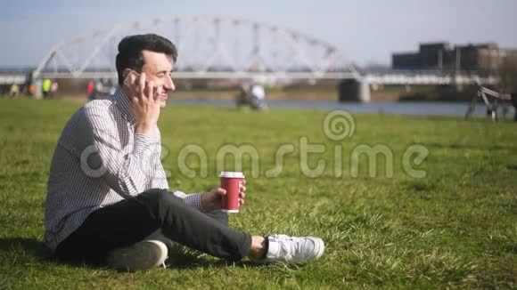 一个人坐在草地上的公园里在打电话学生电话沟通笑笑四处游荡视频的预览图