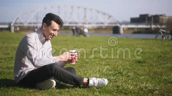 一个写按摩户外和喝咖啡的男人学生坐在草地上聊天英俊的商人和爸爸一起写按摩视频的预览图
