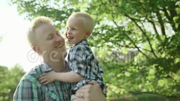 年轻的爸爸和他的儿子一起在夏天的公园里抱着他玩慢速全高清视频的预览图