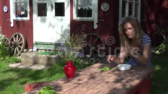 乡村别墅附近的木桌上一个金发女人剥着绿豌豆4K视频的预览图