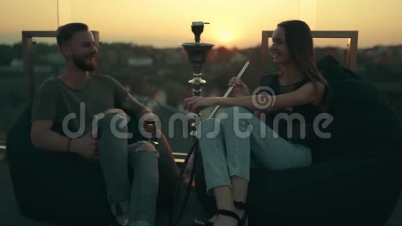 年轻漂亮的一对那个带着女孩的家伙在日落时抽烟笑视频的预览图