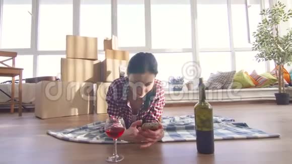 孤独的女孩躺在地上喝酒用智能手机视频的预览图