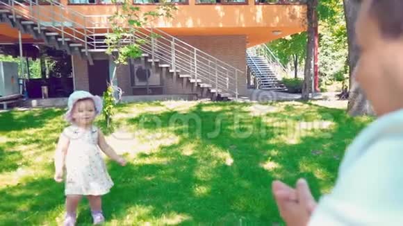 一个小女孩沿着房子附近的绿色草坪慢慢地走到她父亲面前爸爸和女儿笑着视频的预览图