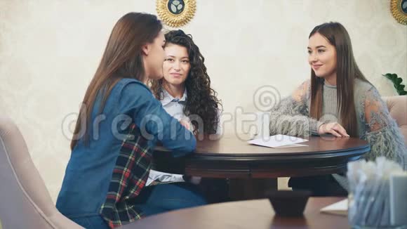快乐的三个漂亮女孩和她们的女朋友坐在咖啡馆里在此期间讲述和讲述各种故事视频的预览图