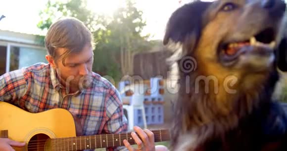 男人和他的狗在花园里弹吉他视频的预览图
