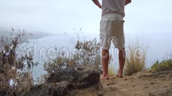 一个站在悬崖边上俯瞰大海的人举起双手在瑜伽的过程中吸入的空气视频的预览图
