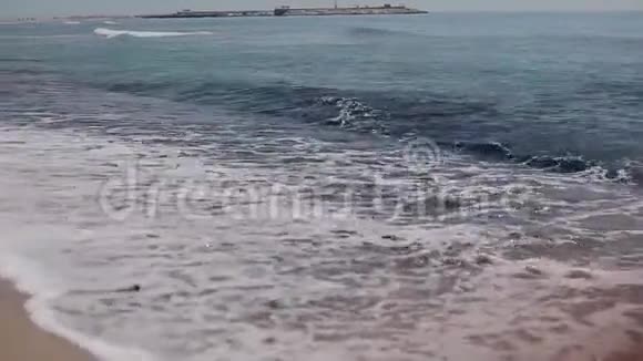 一个苗条美丽的女孩光着脚走在海边的沙滩上的后景视频的预览图