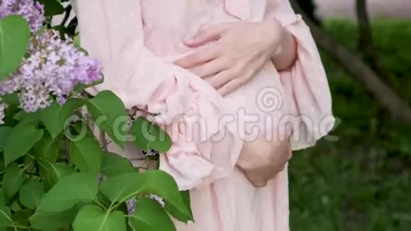 穿粉色连衣裙的孕妇特写腹部一位穿着漂亮衣服的孕妇在公园里散步怀孕了视频的预览图