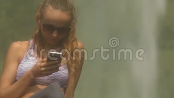 戴墨镜的金发女士通过瀑布特写短信视频的预览图