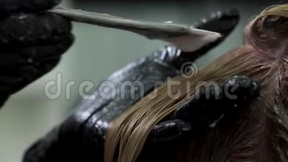 染发师的双手在黑色的辉光中将金色染料涂在头发上视频的预览图