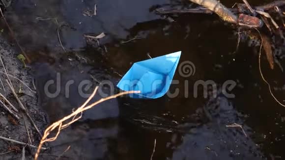 小小的蓝色纸船上流淌着一条透明的河流倒映在其中的树木近点视频的预览图