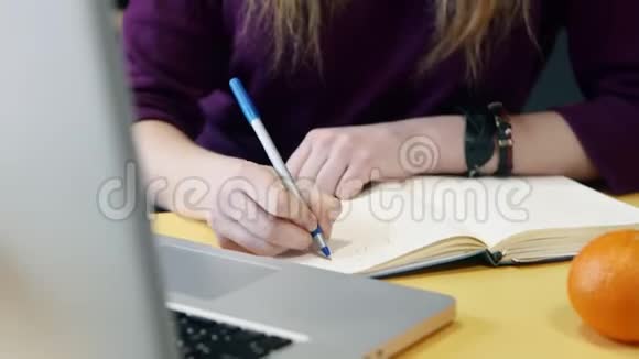 女人在电脑上学习在家里的厨房里用记事本写笔记视频的预览图