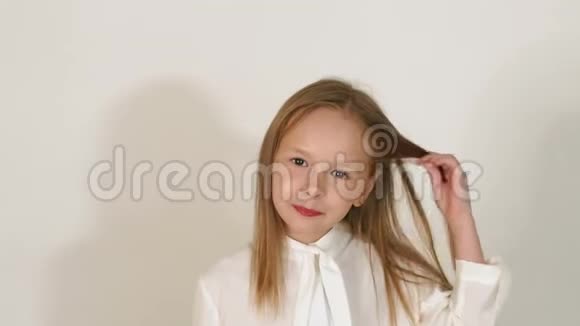 一个穿白色衬衫的金发小女孩在白色墙壁背景上的肖像视频的预览图
