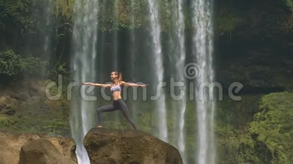 女孩站在瀑布的棕色岩石上做瑜伽姿势视频的预览图