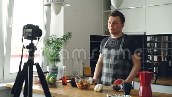 帅哥在家里的厨房里用数码相机录制关于健康烹饪的视频食物vlog记录和记录视频的预览图