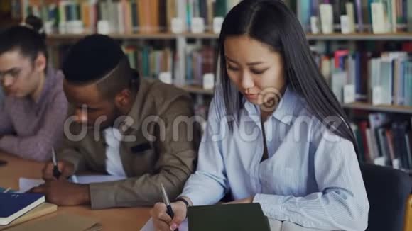 集中亚洲女生准备考试和写笔记坐在大学图书馆的桌子上视频的预览图