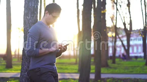 日落时分在公园里的人在城市景观的背景下使用智能手机视频的预览图