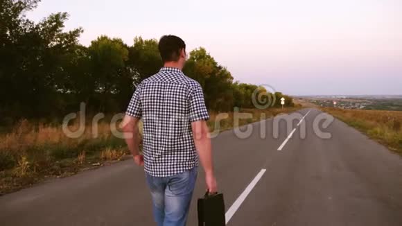 穿格子衬衫的男商人手里拿着一个黑色公文包沿着柏油路走着视频的预览图