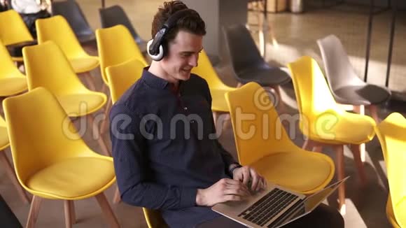 年轻有魅力的家伙在笔记本电脑上工作时正在耳机里随着音乐跳舞视频的预览图