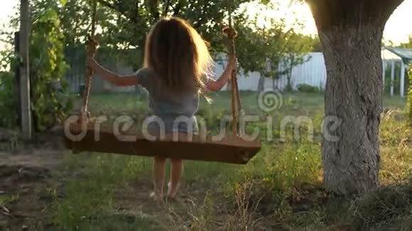 一个留着长发的可爱女孩骑在一个绑在花园里一棵树上的秋千上在村子里休息回忆视频的预览图