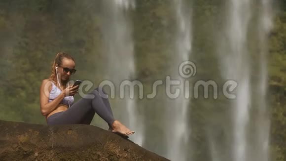 金发女郎光着脚坐在岩石上听音乐视频的预览图