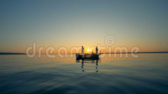 日出时在摩托艇上钓鱼时的男性剪影视频的预览图