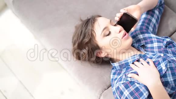 年轻女子在家客厅躺着教练智能手机通讯特写视频的预览图