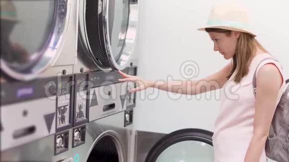 洗衣机房戴帽子的年轻女子阅读如何使用公共洗衣店洗衣服视频的预览图