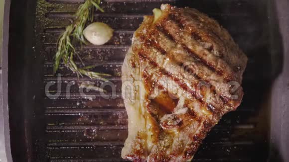 一份牛排是用迷迭香和大蒜在热黑锅上烤的从上面4K的慢动作视频中可以看到视频的预览图
