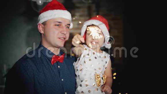 快乐的一家人头戴圣诞老人帽戴着闪闪发光的首饰在圣诞树下微笑视频的预览图