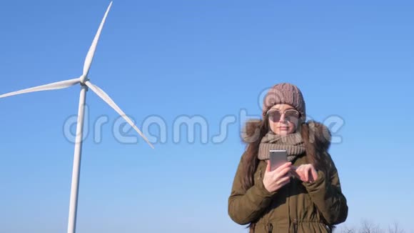 风力发电站微笑的女孩手里拿着智能手机在露天的风车对着天空视频的预览图