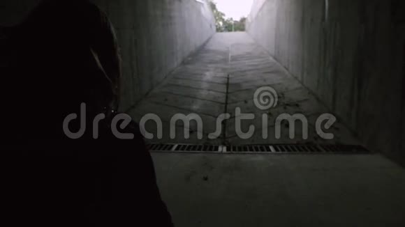 一个年轻的女孩穿过一条黑暗的混凝土隧道走到发光的尽头视频的预览图