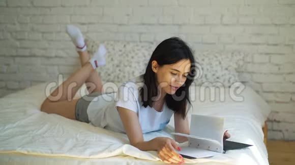 住嘴美丽的黑发女孩躺在床上拿着一本书看书一个年轻的女人打开一本有趣的书视频的预览图