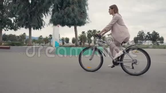 女骑自行车的人在夏天在城市道路上骑自行车侧视视频的预览图