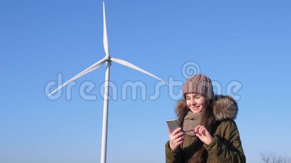 现代技术可爱的女性坐在互联网上使用智能手机旁边的风力涡轮机视频的预览图