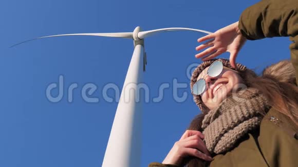 女孩站在风车旋转的涡轮机下在天空特写的背景下眺望远方视频的预览图