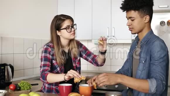可爱的年轻幸福夫妇坐在厨房里互相喂牛角面包一起吃美味的早餐视频的预览图