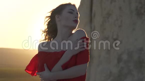 穿着红裙子的年轻女子看着躲在悬崖后面的太阳风摇着她的头发视频的预览图