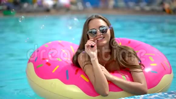 夏天美丽的年轻女子比基尼女孩哈文在洒满甜甜圈的乐趣在游泳池假期夏天夏天视频的预览图