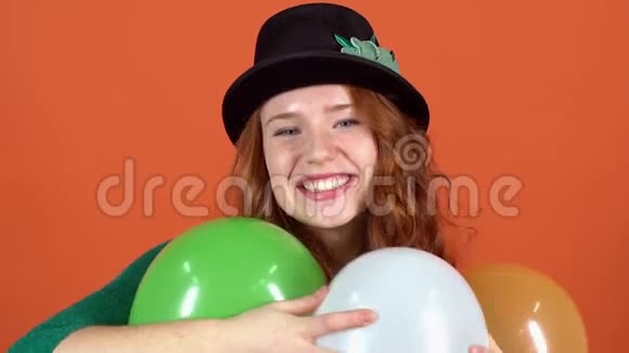 年轻女子庆祝圣帕特里克节橙色墙上戴着帽子拥抱气球视频的预览图