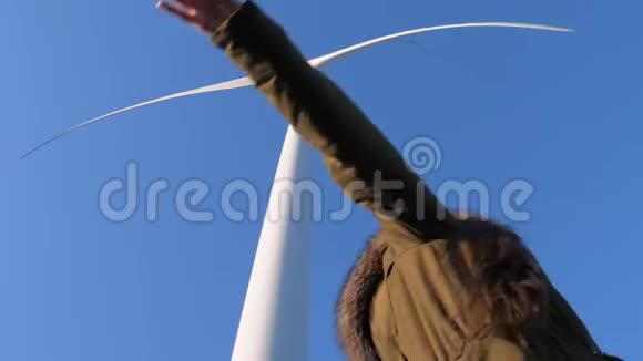 快乐的女人在风力发电机的特写镜头下享受乐趣挥舞着手臂对抗天空视频的预览图