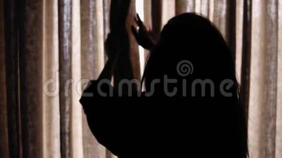 一个女性剪影打开窗帘让光线进入房间的慢镜头背面视频的预览图
