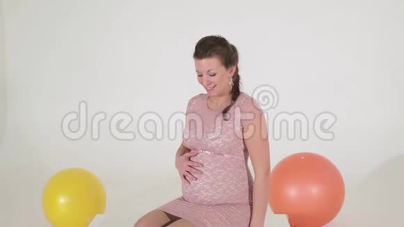 穿着粉色裙子的成熟孕妇坐在镜头前摸胃视频的预览图