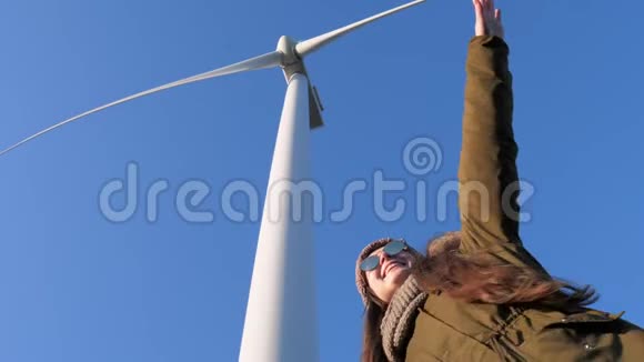 戴着眼镜的快乐女孩挥舞着双手在风力发电站的特写镜头下与天空嬉戏视频的预览图
