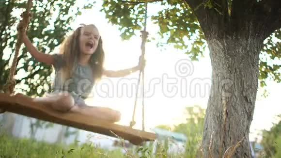 长头发的赤脚女孩在夕阳的映衬下骑在花园里的秋千上她把脚视频的预览图