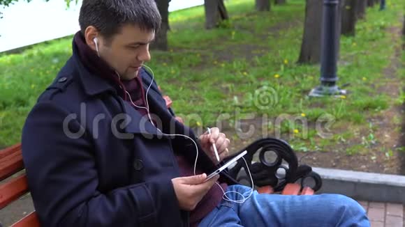 一个人听音乐在公园里的平板电脑上工作视频的预览图