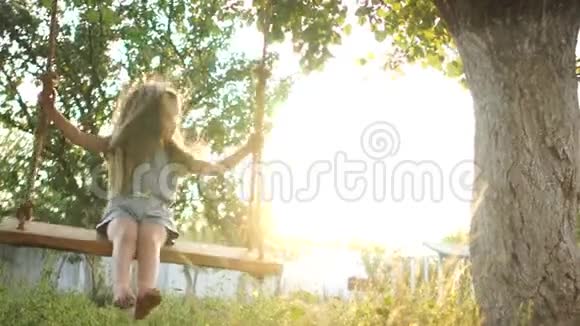 在夕阳的映衬下一个四岁的长发女孩骑在花园里的秋千上节日快乐视频的预览图