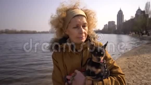 一位成年金发卷发白人妇女的肖像她手里拿着一只黑色的小狗种玩具猎犬老搞笑视频的预览图